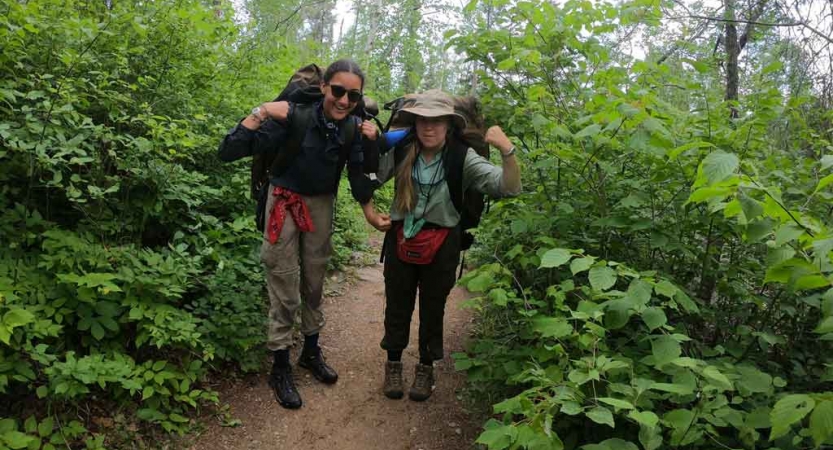 two students wear backpacks and flex their arm muscles on an outward bound course in minnesota